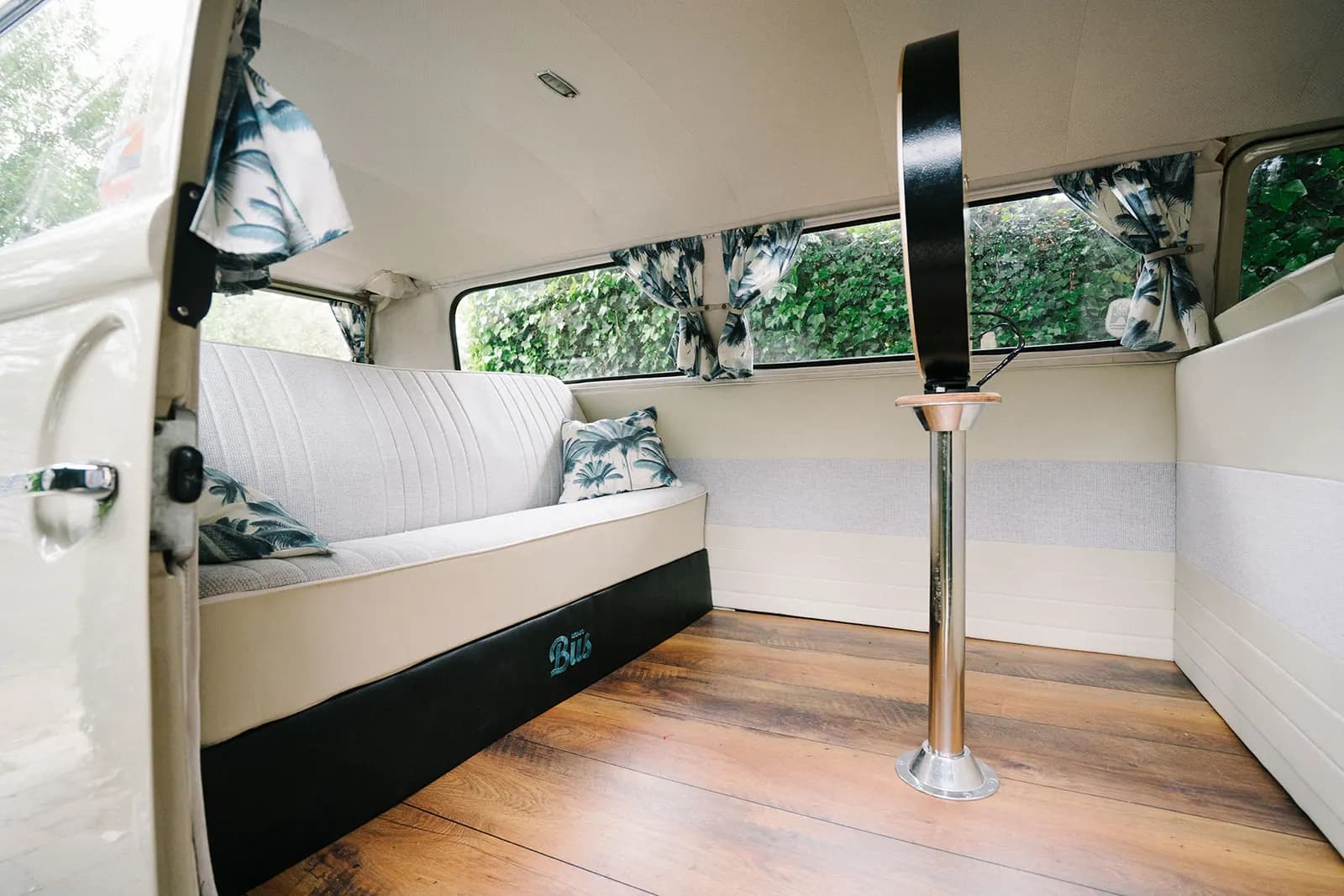Interior with light-coloured back seat, palm-print cushions, wooden floor and photo booth with ring light