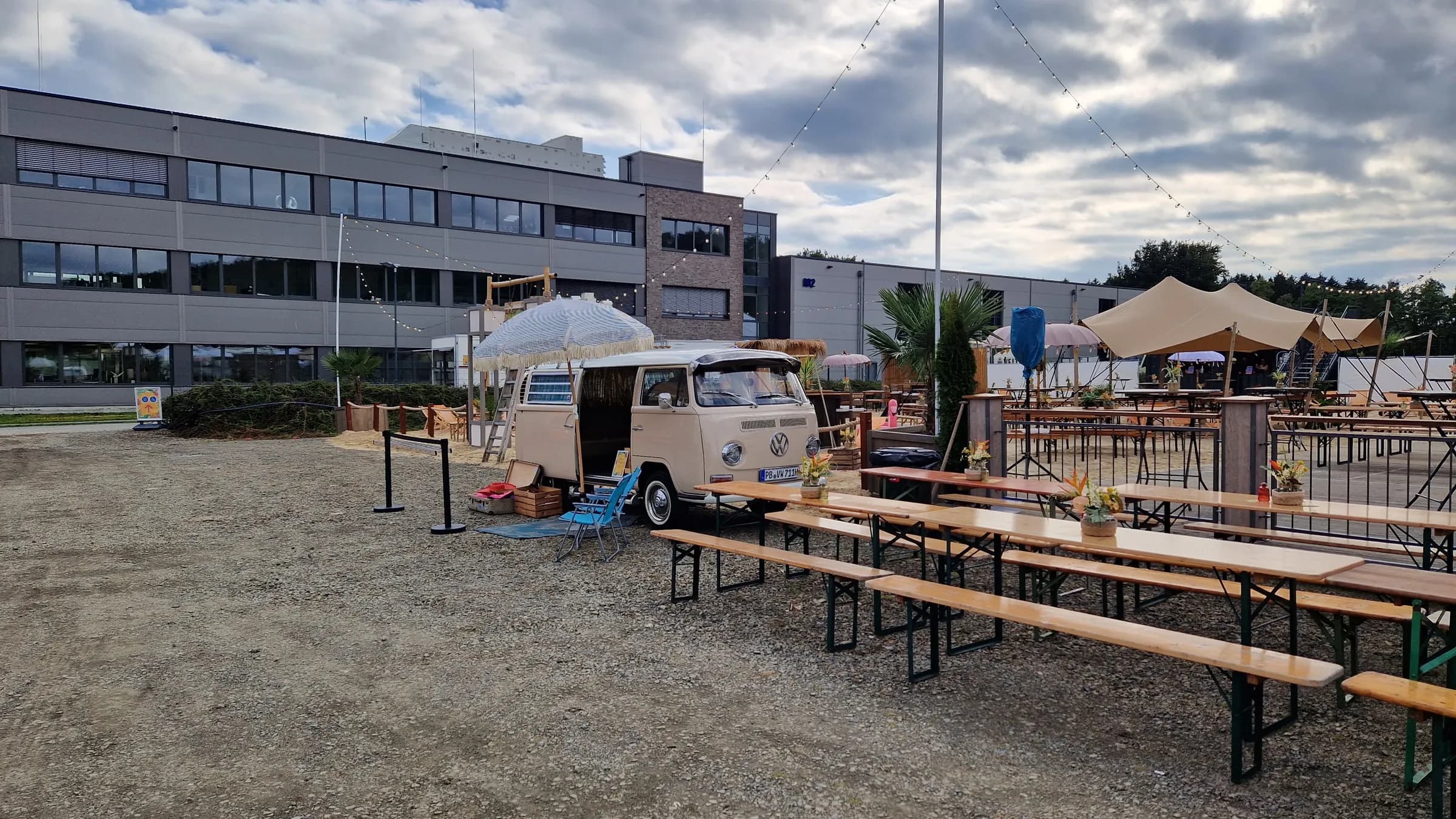 Photo booth bus with a parasol in front of an office building, next to long rows of beer tables and fairy lights for the company party