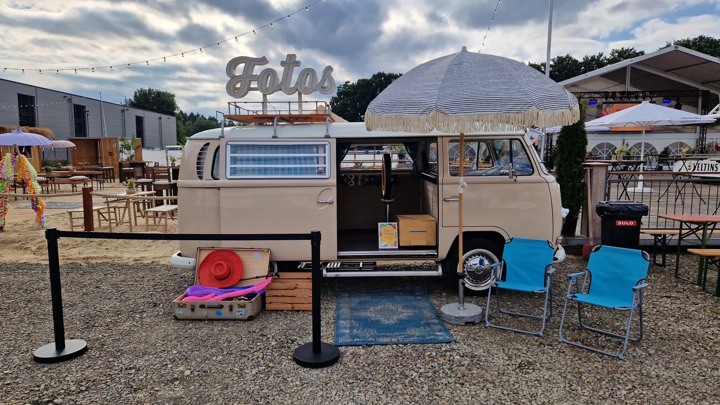 Photo booth bus with its sliding door open, photo booth, props case, rug and blue folding chairs behind a barrier