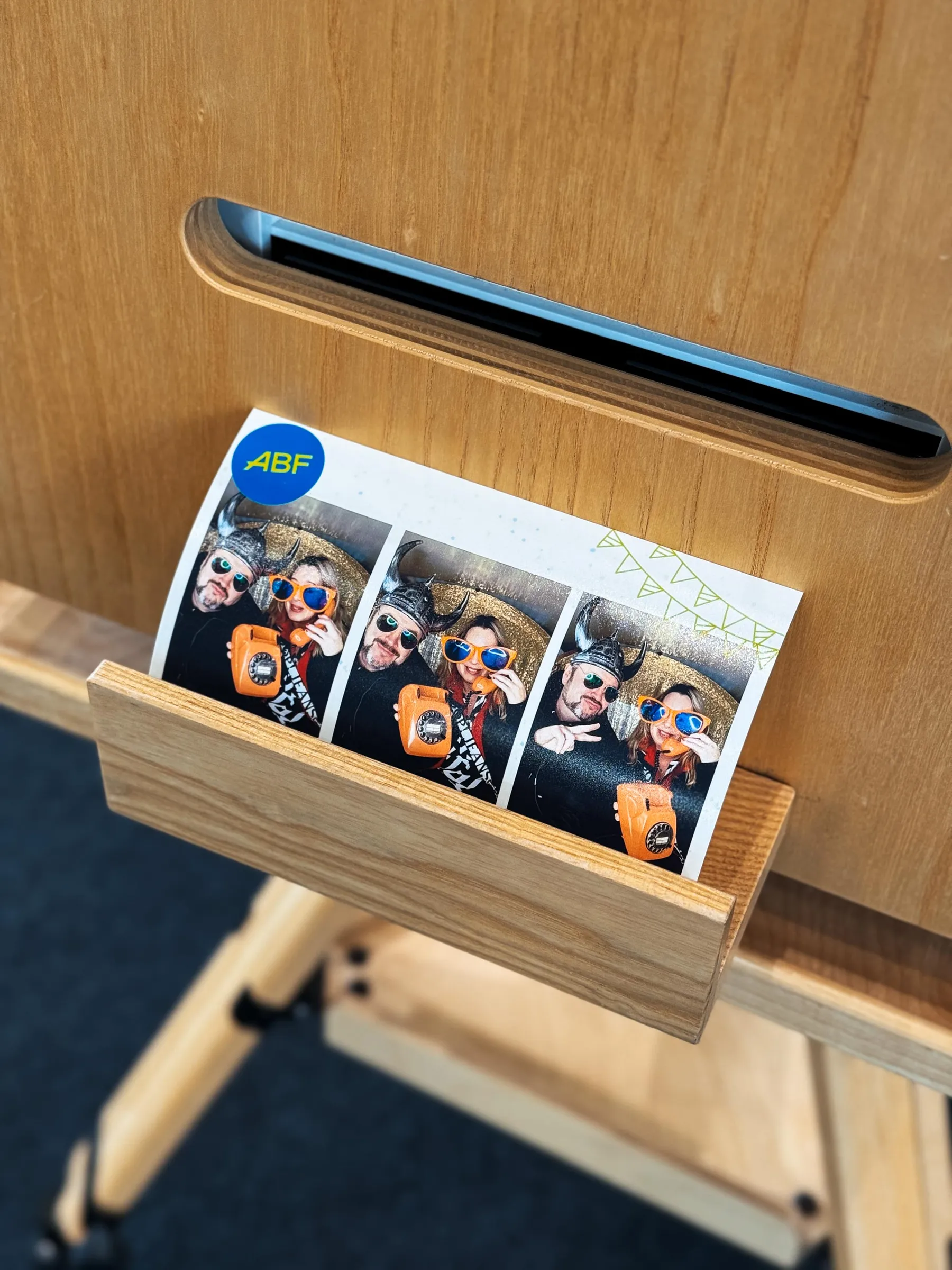 Ausdruck mit ABF-Logo in der Holzablage am Fotobulli-Drucker: zwei Gäste mit Wikingerhelm, XXL-Brille und orangem Telefon