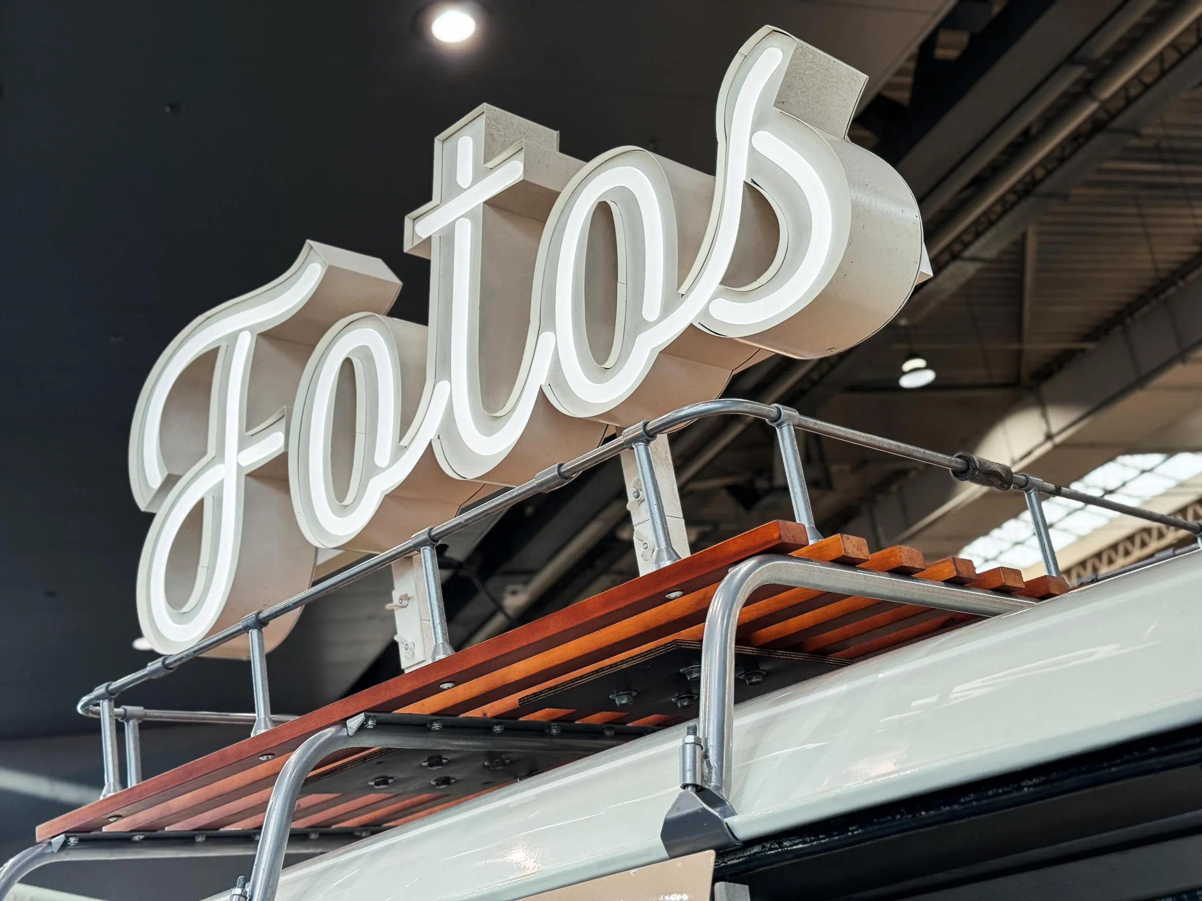 Weiß leuchtender Schriftzug „Fotos“ auf dem Dachgepäckträger mit Holzlatten des Fotobullis in der Messehalle