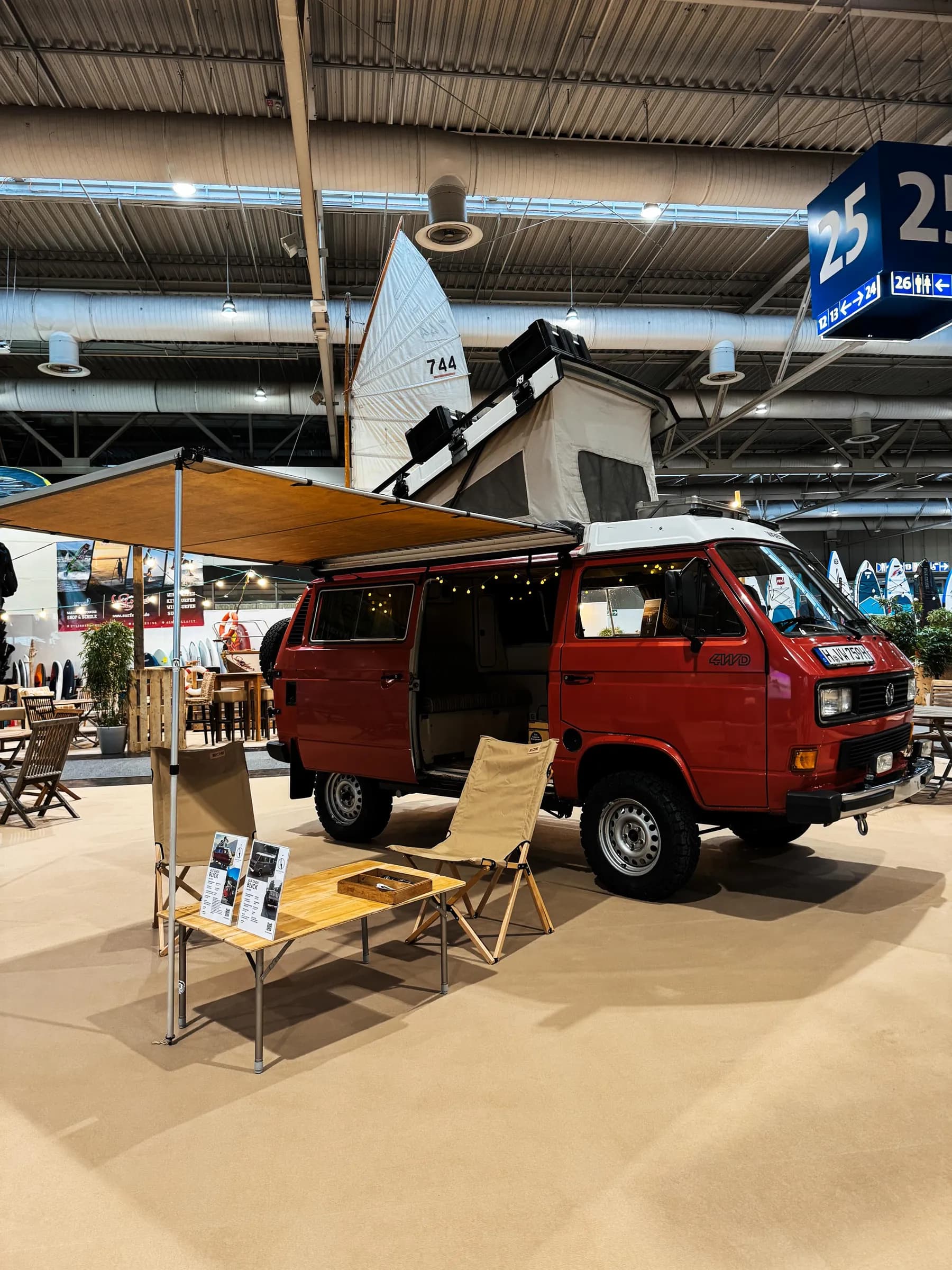 Roter VW-Bus mit Aufstelldach und Markise, davor Campingtisch und Stühle auf einem Stand in Halle 25 der ABF