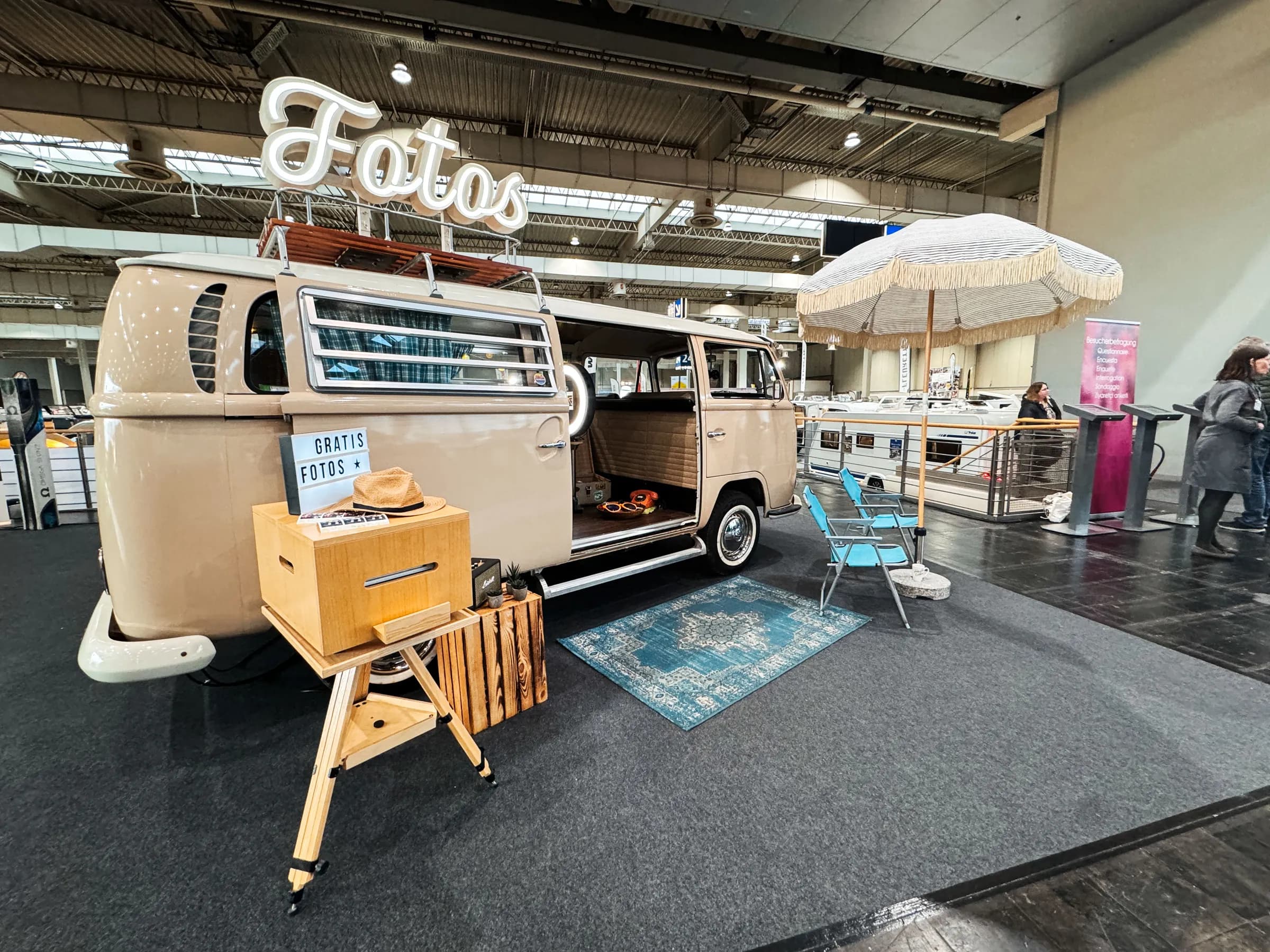 Beiger Fotobulli mit Leuchtschrift „Fotos“, Sonnenschirm, Teppich und Drucker auf einem Messestand der ABF in Hannover