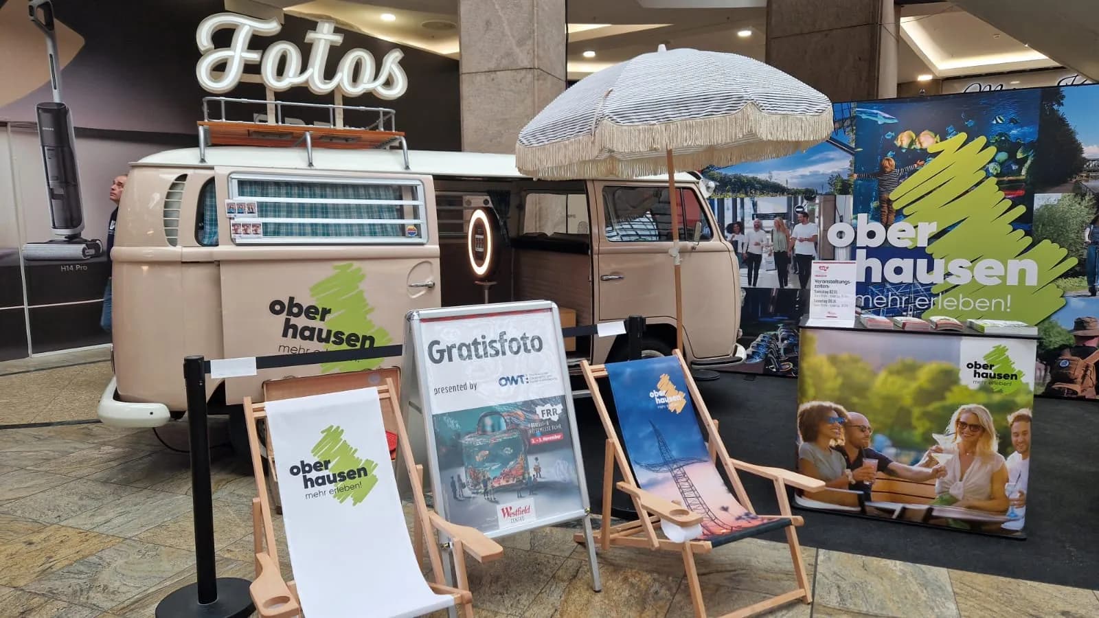 Fotobulli mit „Fotos“-Leuchtschrift, Sonnenschirm und Liegestühlen am Oberhausen-Stand der FFR im Einkaufszentrum