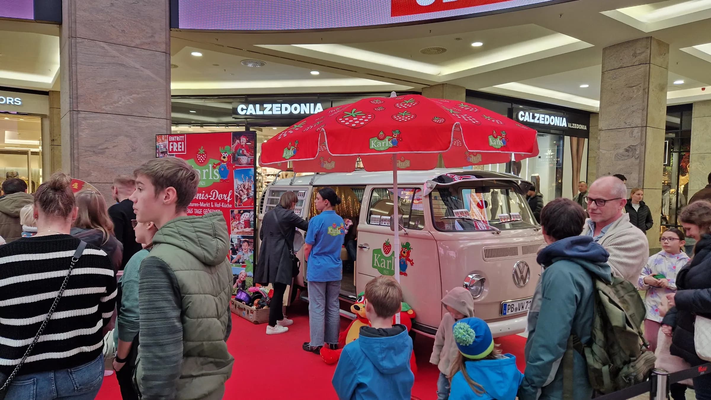 Photo booth bus in Karls design on a red carpet, female host at the sliding door, children and adults waiting in front
