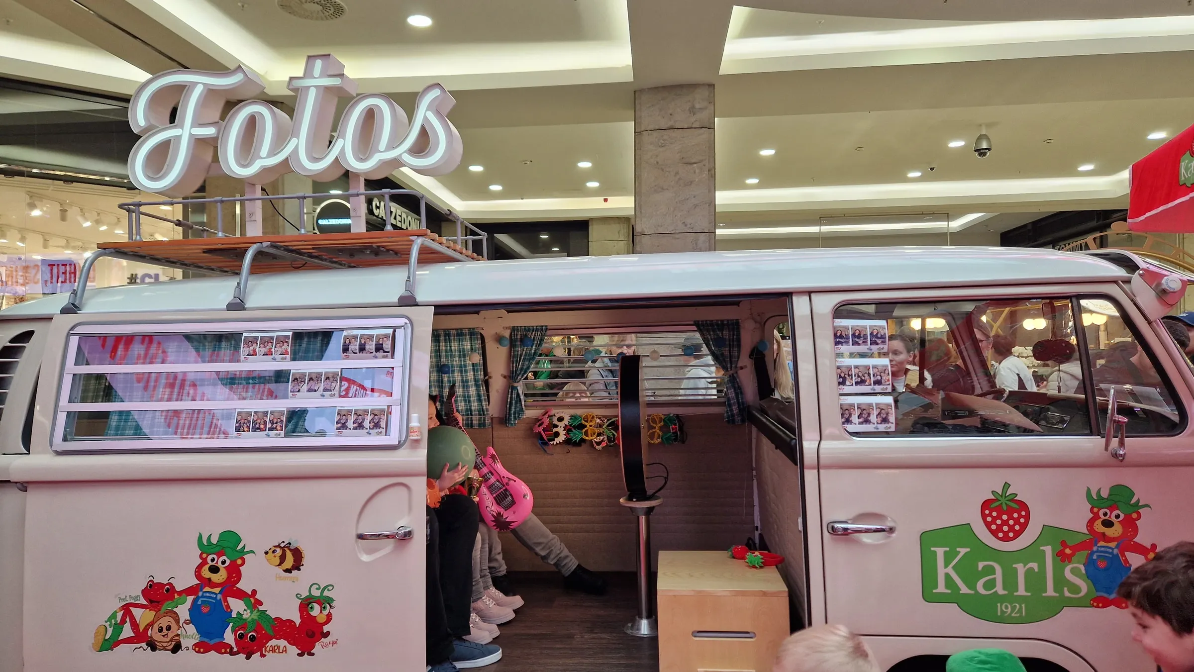 Photo booth bus with its sliding door open, photo strips in the windows, props inside and an illuminated ‘Fotos’ sign on the roof