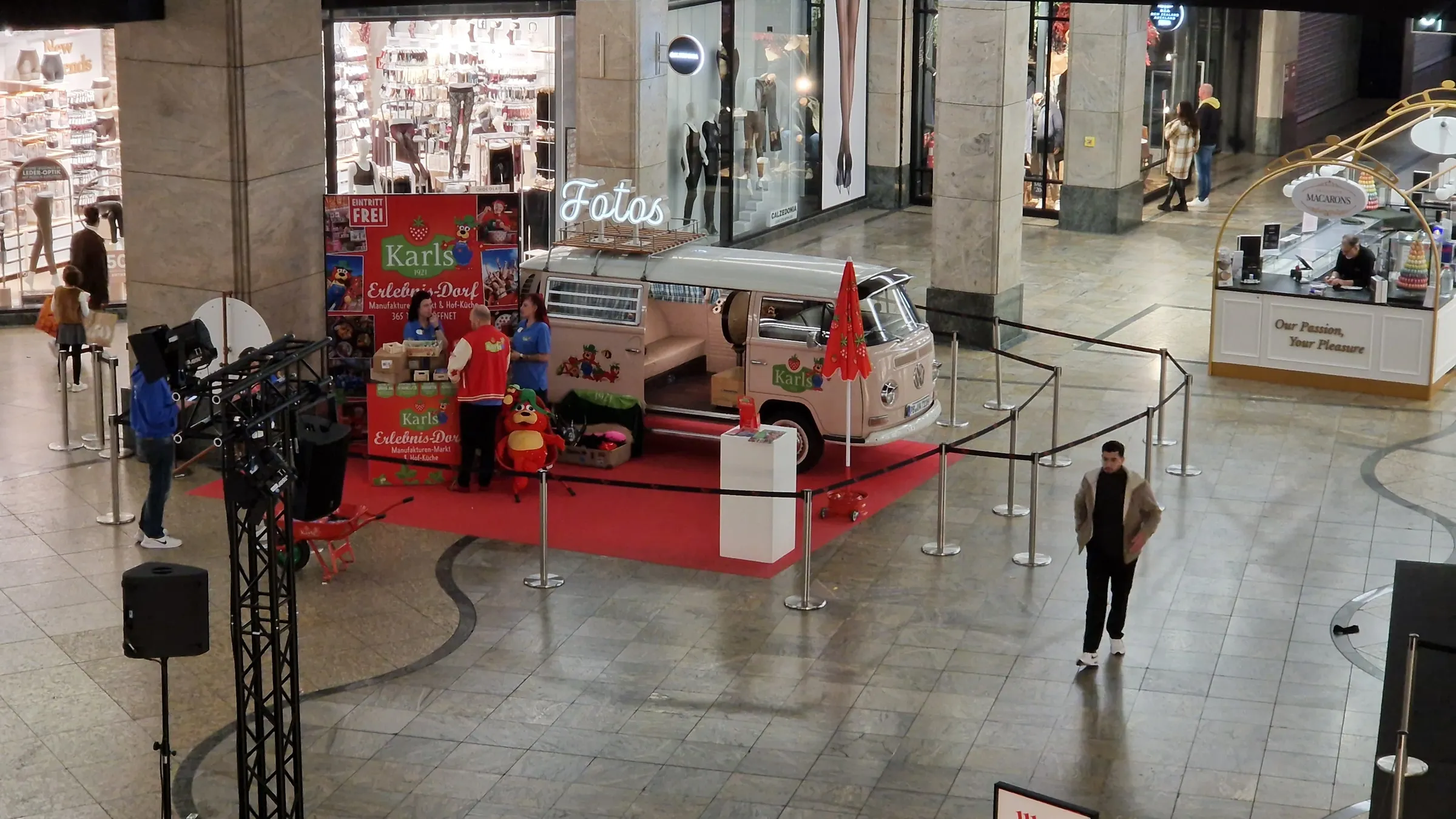 Photo booth bus with Karls branding on a red carpet in a shopping centre, next to an information stand and a barrier