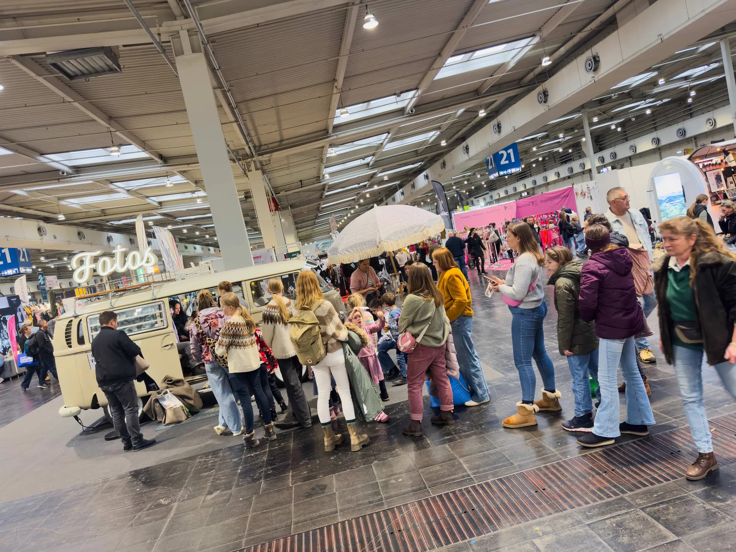 Lange Schlange vor dem Fotobulli mit Leuchtschrift „Fotos“ und Sonnenschirm in Halle 21 der Passion Pferd 2025