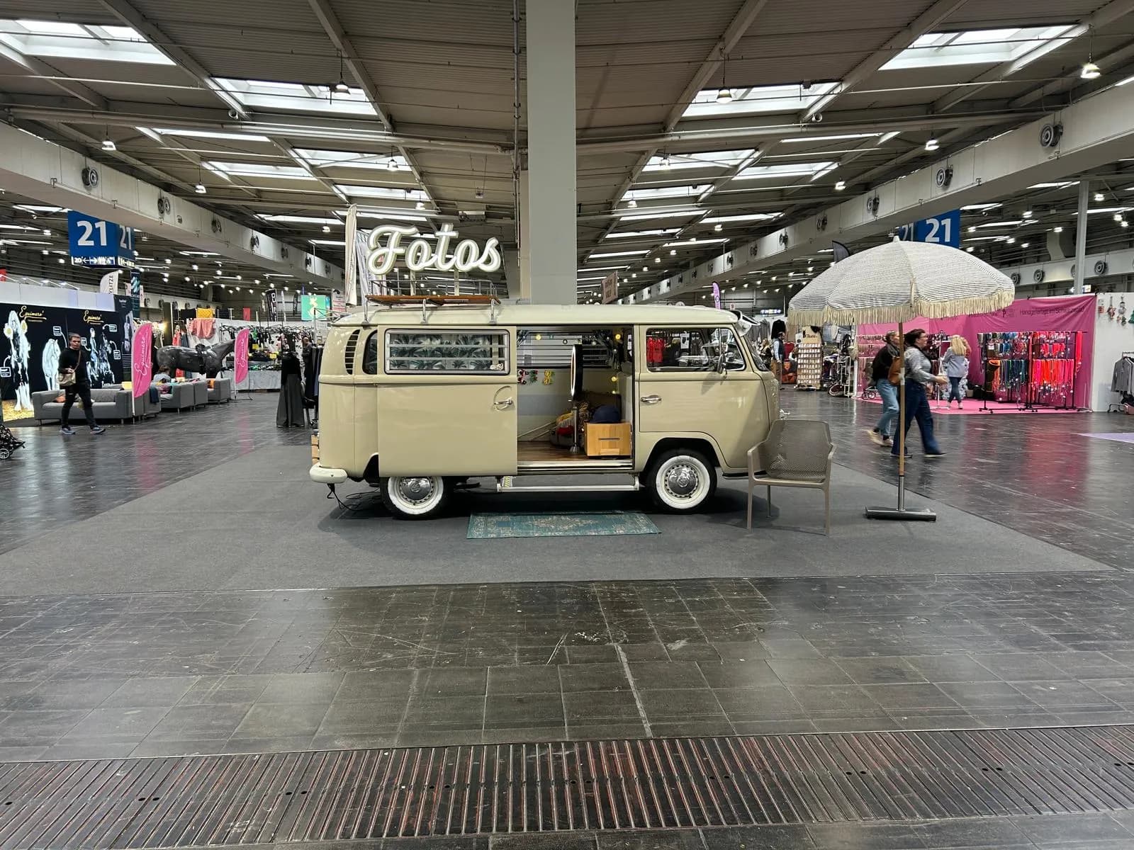 Beigefarbener Fotobulli mit offener Schiebetür, Leuchtschrift „Fotos“, Sonnenschirm und Teppich in Messehalle 21