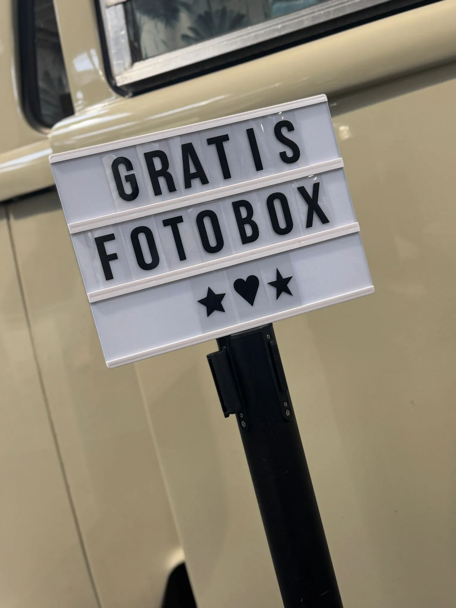 Leuchtschild mit der Aufschrift „Gratis Fotobox“ und Herzsymbol vor der beigefarbenen Seitenwand des Fotobullis