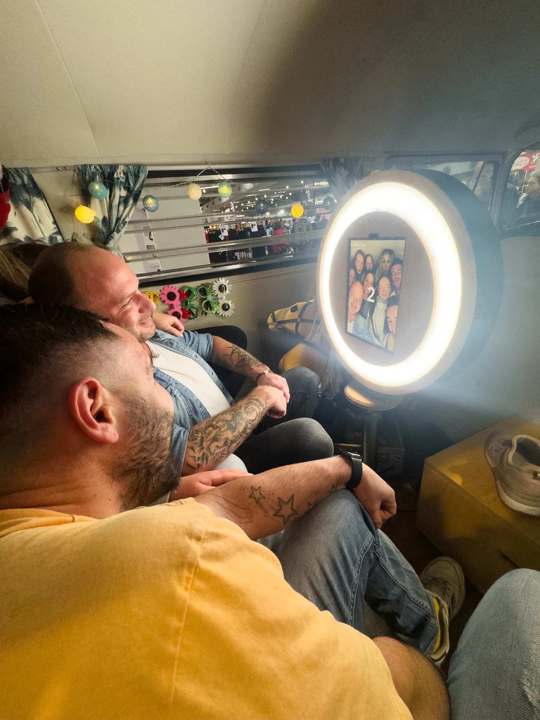 Gäste sitzen im Fotobulli vor der Fotobox mit Ringlicht, das Display zeigt einen Countdown und das Gruppenbild