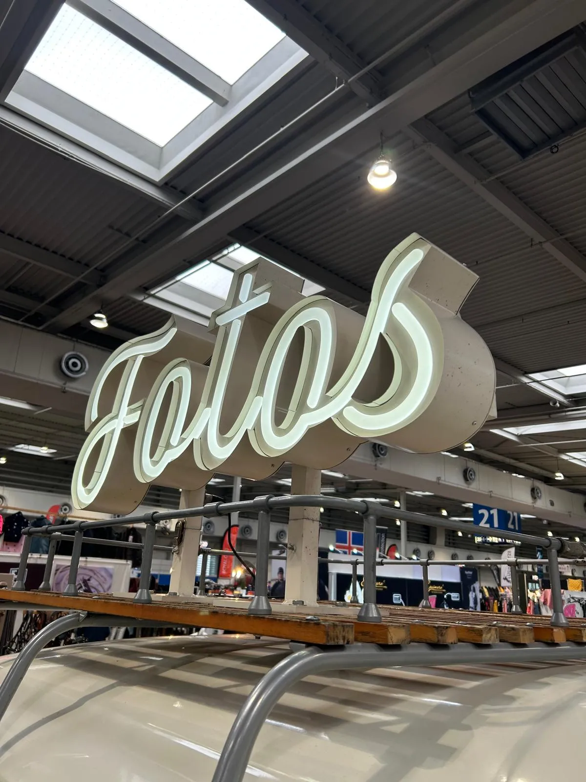 Leuchtschrift „Fotos“ auf dem Holz-Dachträger des Fotobullis unter der Hallendecke einer Messe