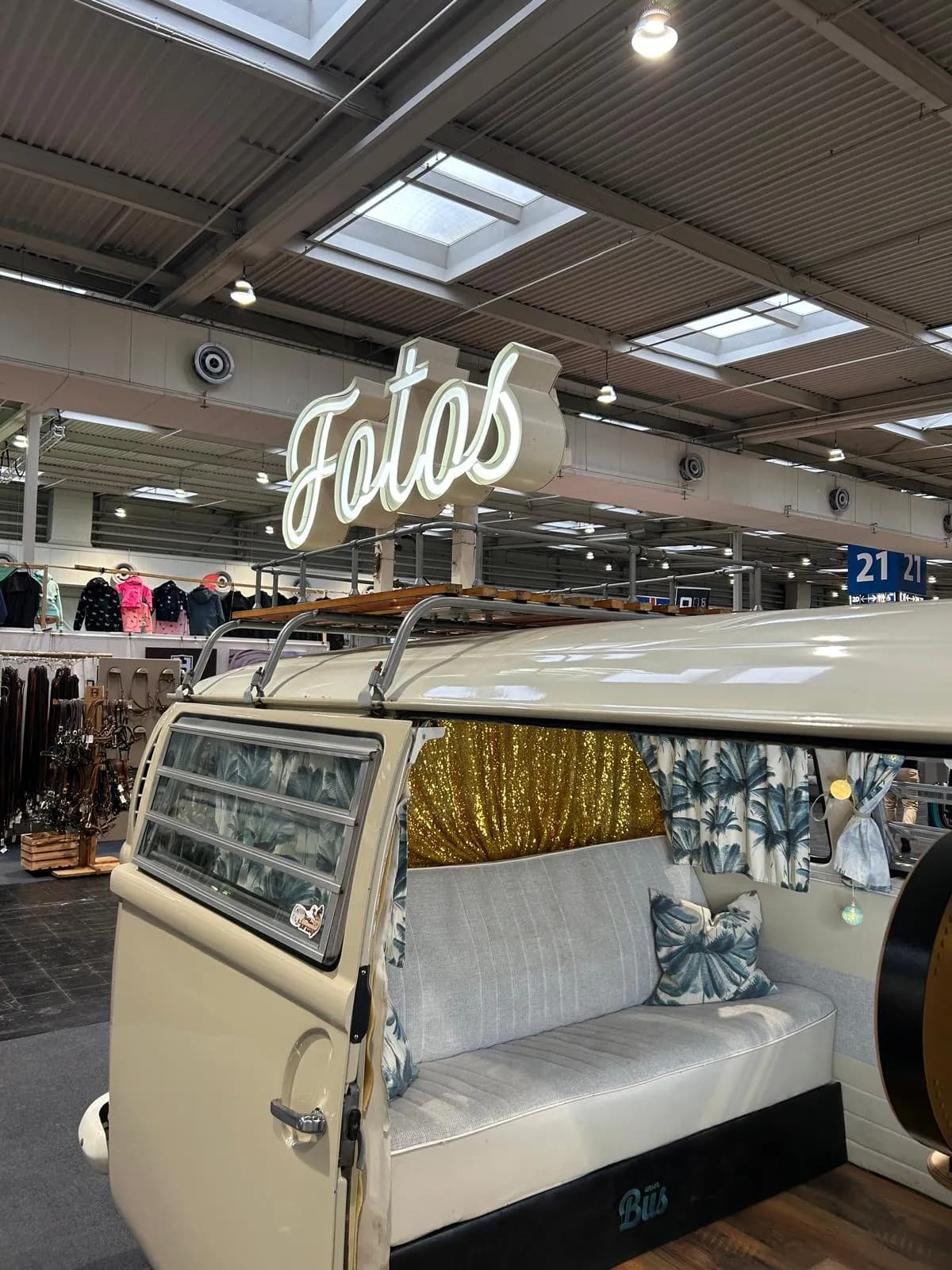 Fotobulli mit leuchtendem „Fotos“-Schriftzug auf dem Dachträger und offener Schiebetür in einer Messehalle