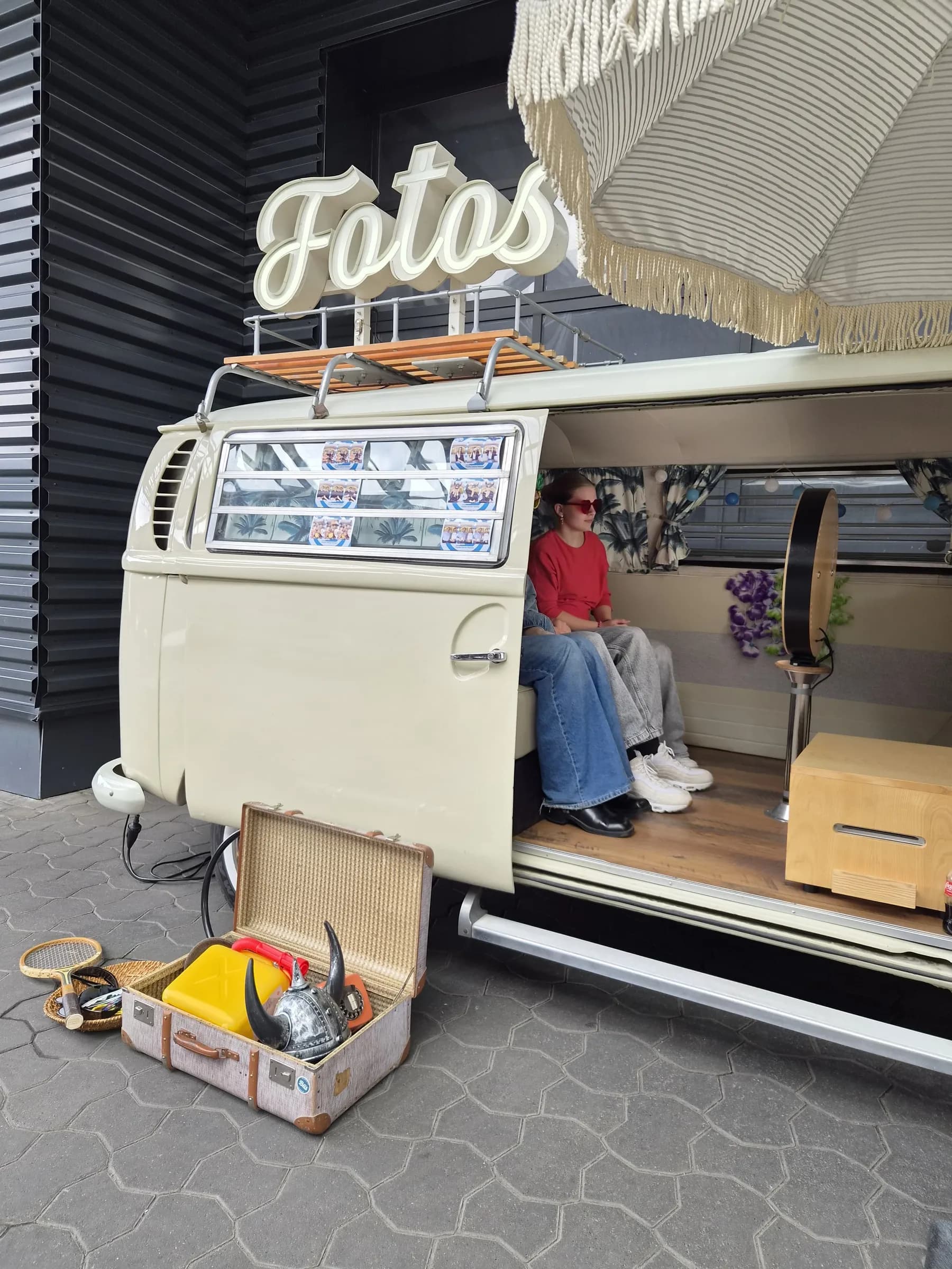 Guests sitting in the open photo booth bus in front of the photo booth, with an old suitcase holding a Viking helmet and props in the foreground