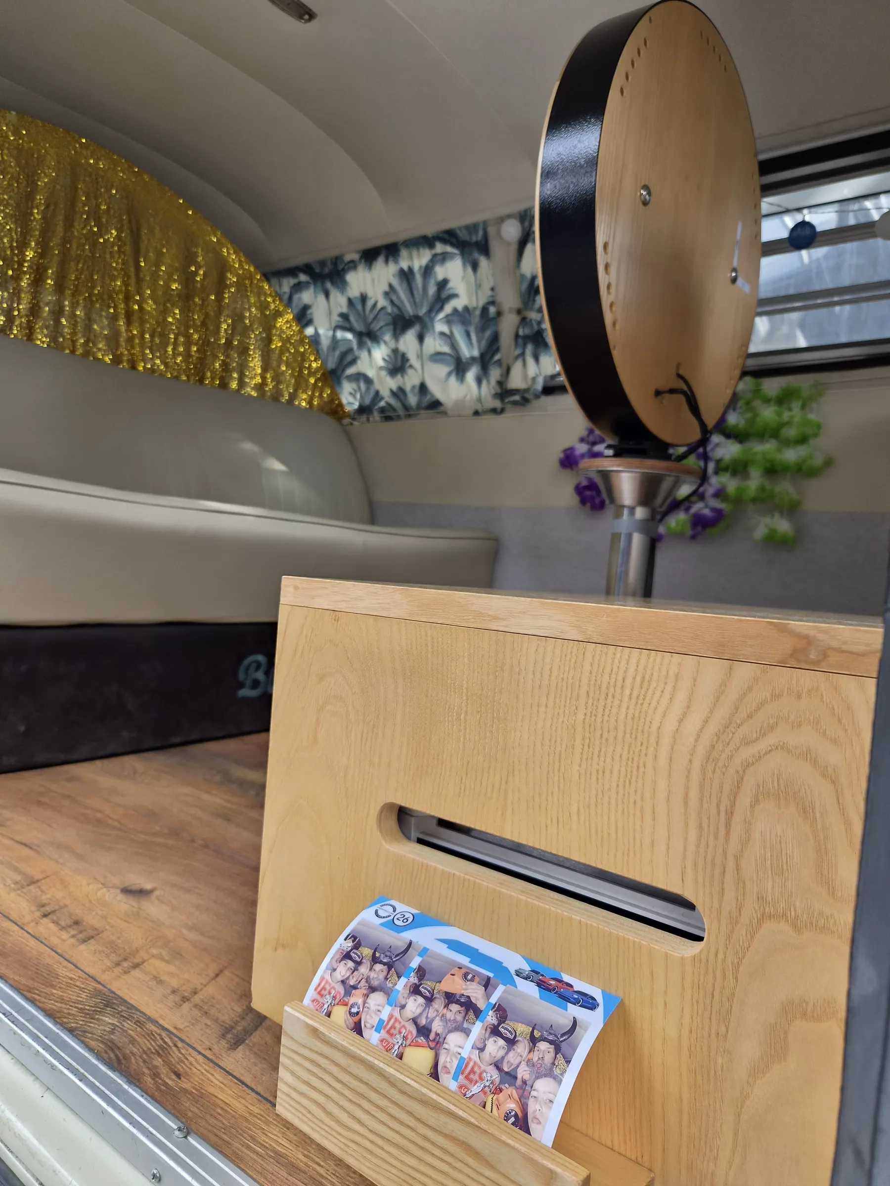 Interior of the photo booth bus with a bench seat, glitter curtain, round wooden photo booth and a fresh photo strip in the holder