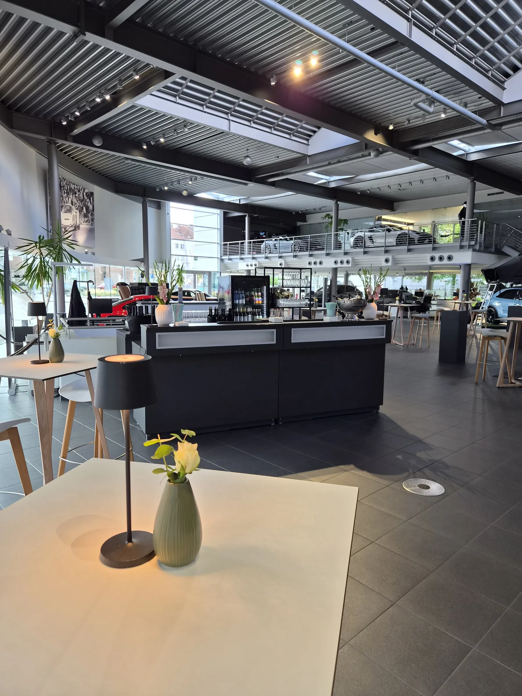 Showroom of Porsche Zentrum Hannover with a bar, poseur tables and sports cars on the gallery