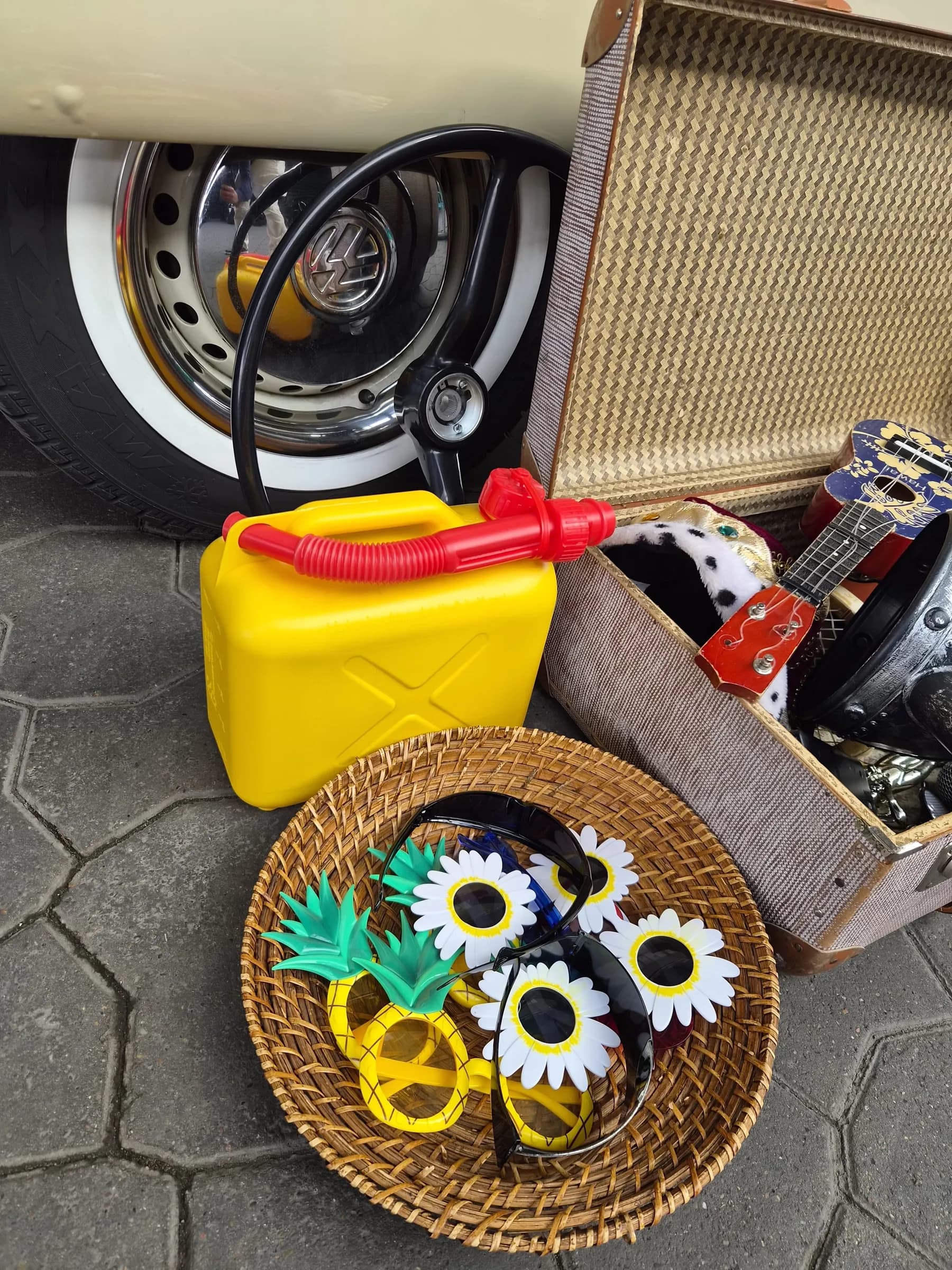 Props in front of the wheel of the photo booth bus: yellow jerrycan, steering wheel, basket of novelty glasses and an old suitcase with a ukulele