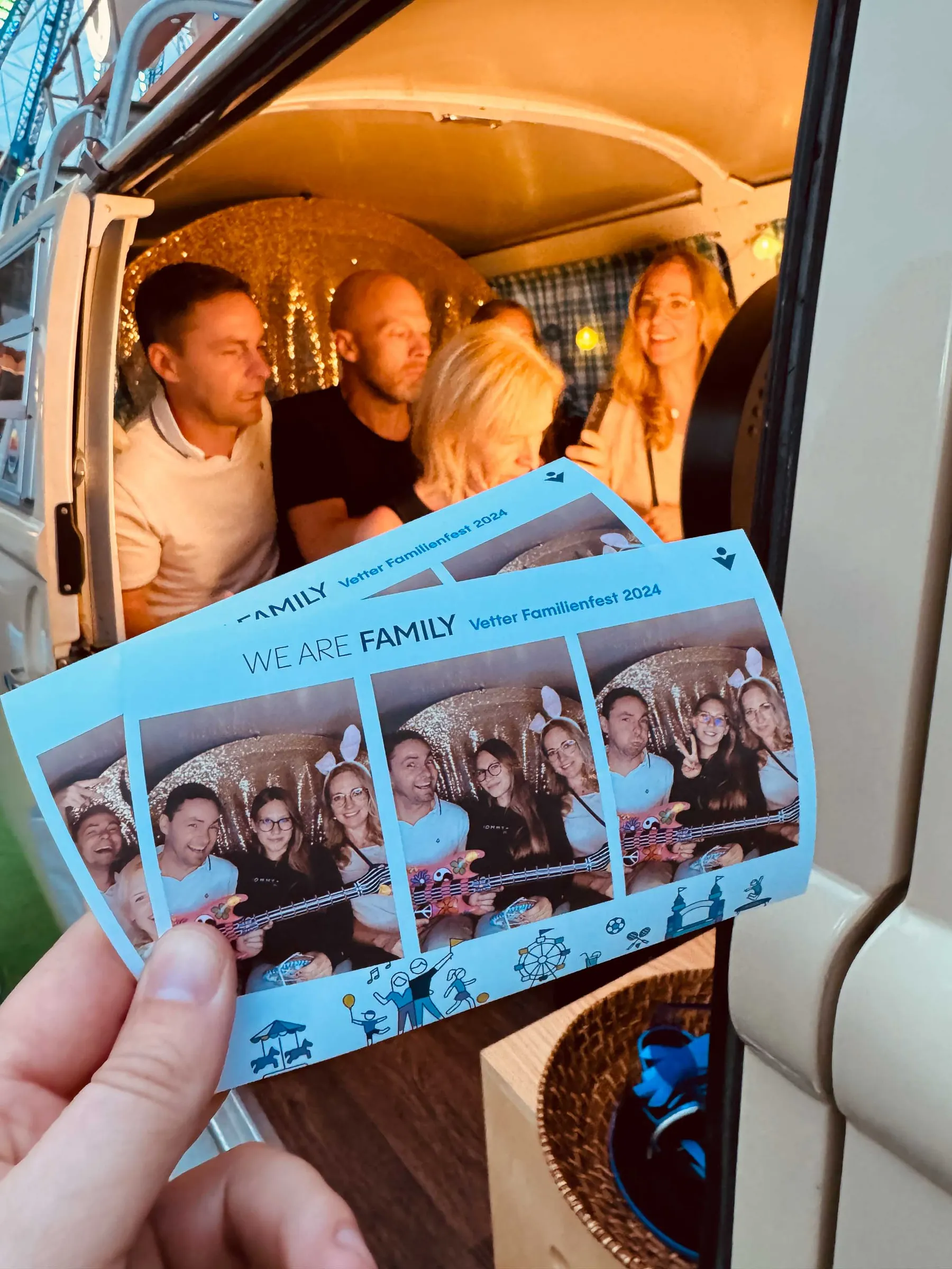 Hand hält Fotostreifen im Event-Design, dahinter posieren Gäste im beleuchteten Innenraum des Fotobullis