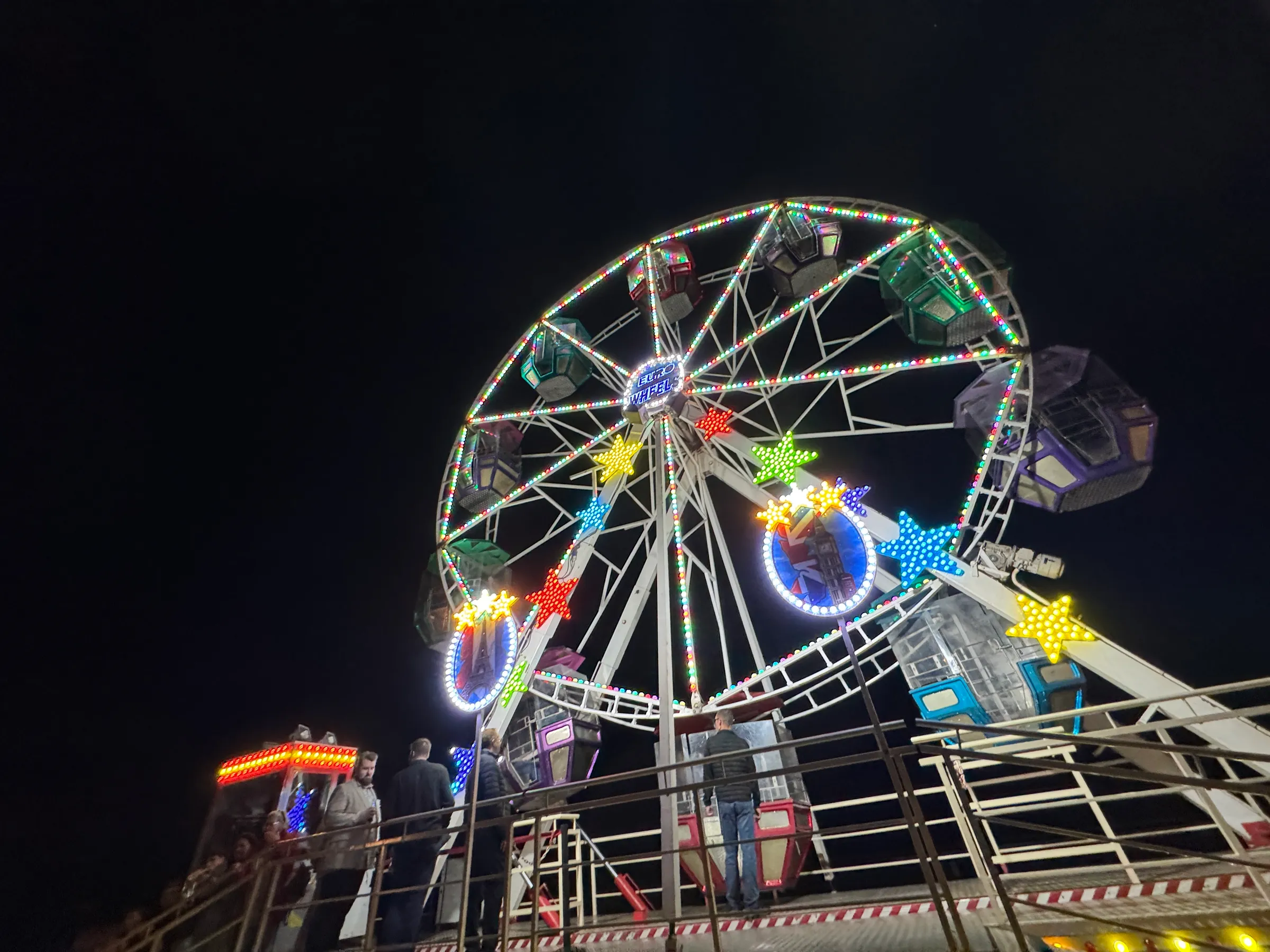 Colourfully lit Ferris wheel with stars at night, with guests in front at the VHV Versicherungen summer party