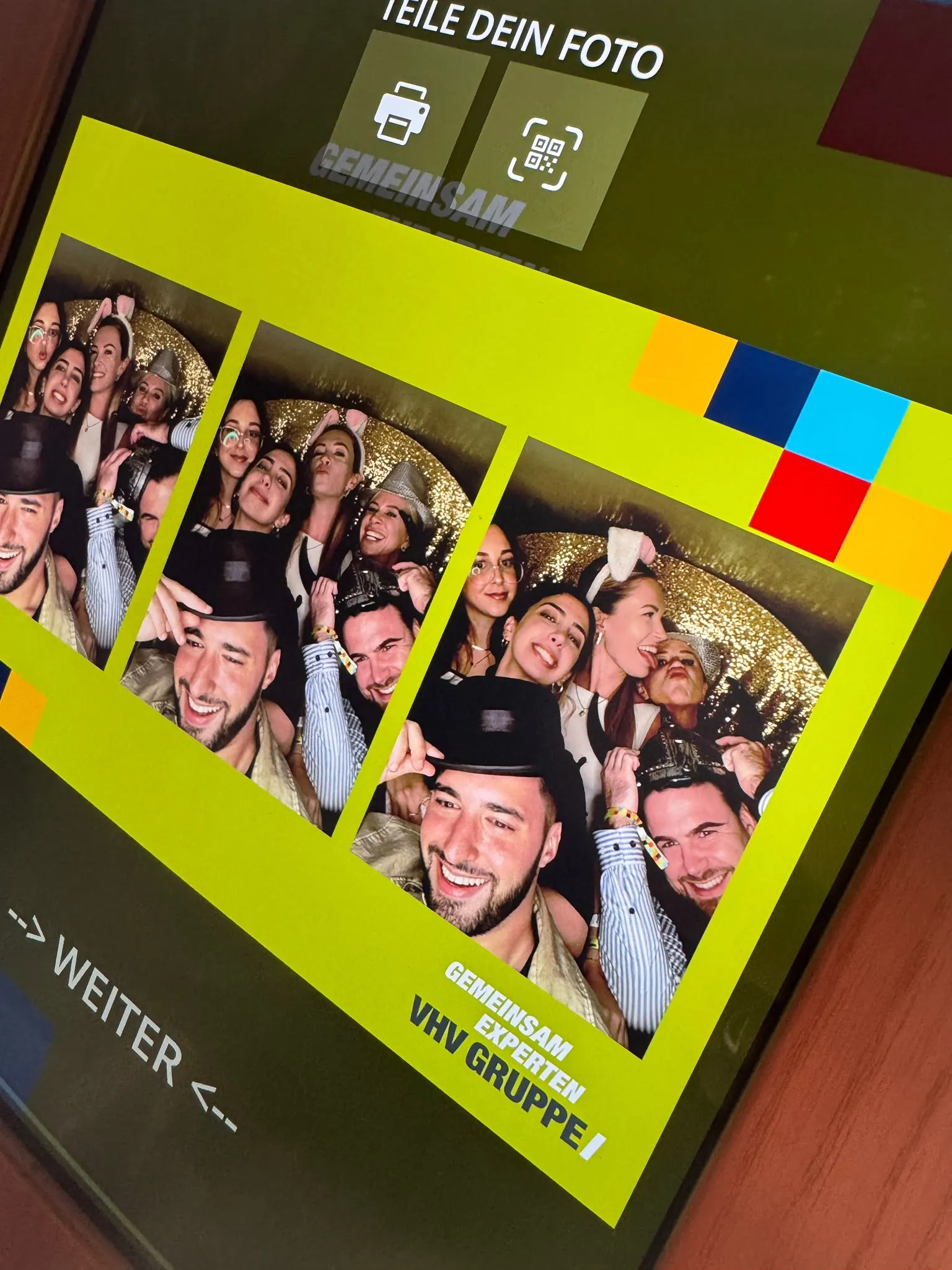 Display of the photo booth inside the Bulli showing a photo strip of laughing guests in the VHV Gruppe layout, with print and QR code